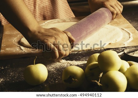 Girl makes an apple pie, rolls the dough. Apples on the table.Toned, Vintage. Hands in picture.