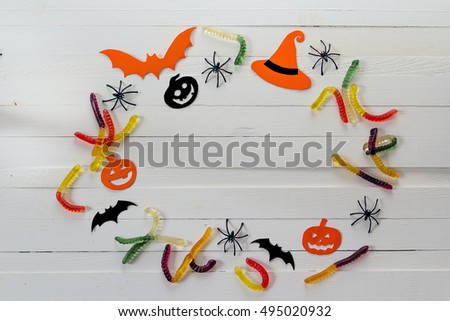 Halloween background with frame of jelly worms, paper pumpkins and decorative spiders. Space for text.