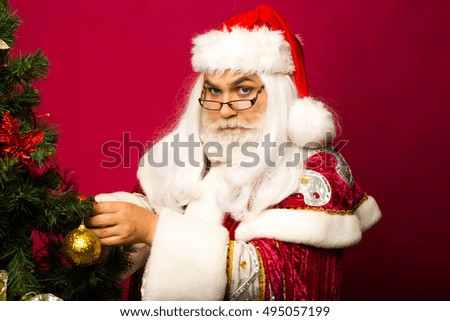 Santa claus man in eyeglasses with white beard in new year red suit decorates Christmas tree