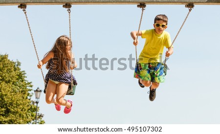 Fun and joy of children. Little girl and boy playing outdoor on preschool playground garden. Kids swinging on swing-set to touch the sky. Royalty-Free Stock Photo #495107302