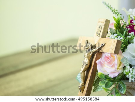 The crucifix of Jesus with flowers over burred wooden table and yellow background with copy space
