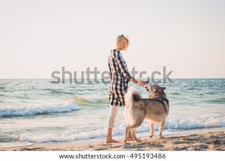 Young female walking with siberian husky dog on sea front at sunrise