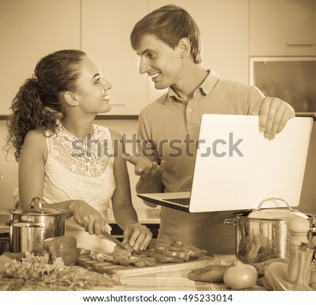 Smiling young guy showing cooking girlfriend something on laptop screen