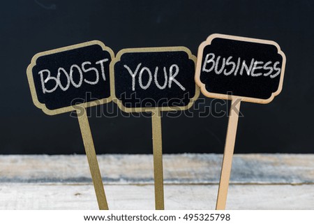 BOOST YOUR BUSINESS message written with chalk on wooden mini blackboard labels, defocused chalkboard and wood table in background
