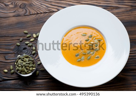 White glass plate with pumpkin cream-soup over wooden background