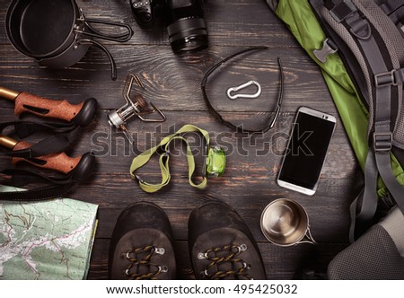 Hiking accessories. Boots, backpack, sunglasses, photo camera, map, smartphone, flashlight and others. Top view. 