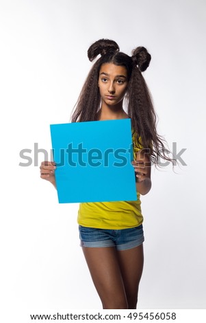 Emotional young brunette girl with long hair in yellow t-shirt with a blue sheet of paper for notes on a white background