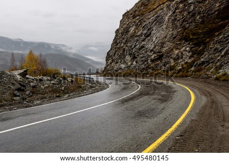Scenic view of the hairpin bend wet winding road through the pass, part of the mountain serpentine in autumn cloudy weather with fog