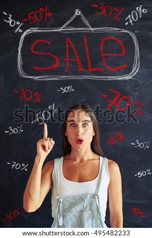 Happy and excited look of beautiful young woman standing against blackboard with chalk inscriptions of sale