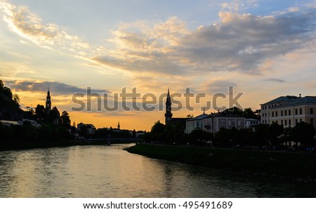 Magic great view on an evening city shining in the lights of sunset - dramatic picture. Beautiful clouds over Salzach river and promenade with the resting people. Salzburg, Austria