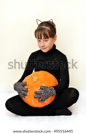 Lovely fair-skinned girl with green eyes in Halloween costume of black cat with pumpkins on a light background