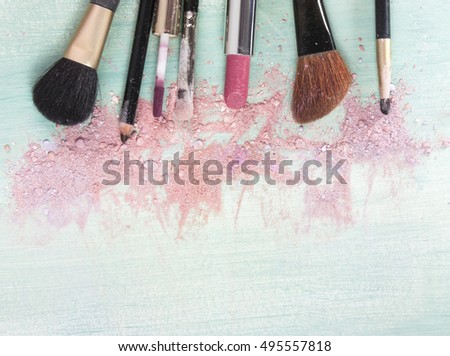 Makeup brushes and lipstick on a teal blue background, with traces of powder and blush on it. A horizontal template for a makeup artist's business card or flyer design. With plenty of copyspace