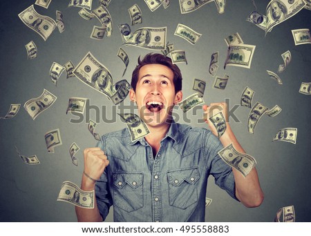 Happy young man screaming super excited. Portrait ecstatic guy celebrates success under money rain falling down dollar bills banknotes isolated gray background. Financial freedom concept