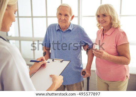 Beautiful young female doctor is talking to old couple and making notes