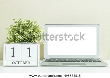 White wooden calendar with black 11 october word with white blank space at center of computer notebook on white wood desk and cream wallpaper textured background , view more date in my portfolio