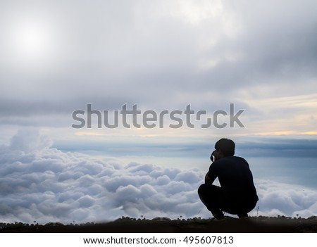 Filtered color and vintage effect of man sitting taking photos on mist on mountain; travel concept, morning light