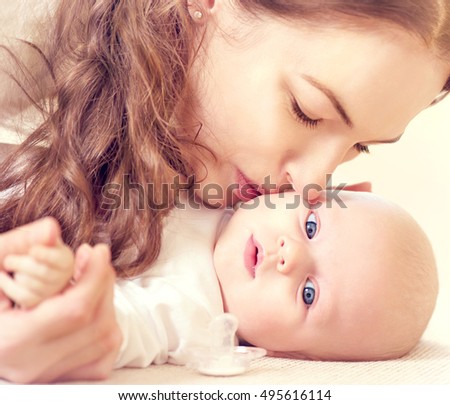 Mother and her Newborn Baby together. Love. Happy Mother and Baby kissing and hugging. High key soft image of Beautiful Family. Maternity concept. Parenthood. Motherhood