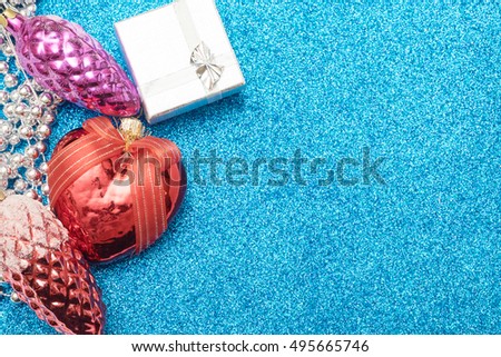 Three christmas toy bump, christmas heart shaped red ball and small gift box on blue background. Empty space for text.