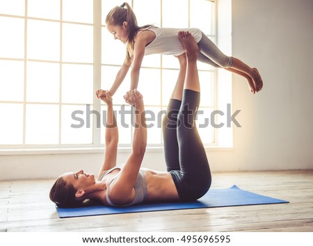 Beautiful young woman and charming little girl are smiling while doing yoga together in fitness hall Royalty-Free Stock Photo #495696595