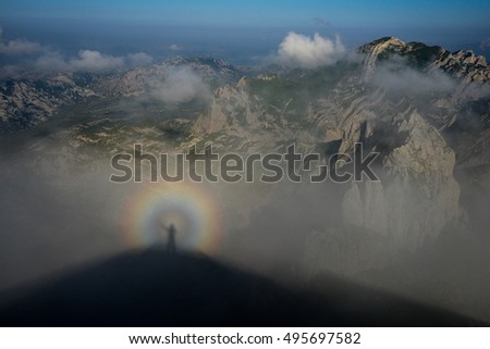 Rainbow-man. Rainbow effect on the photographer silhouette made on the climbing cloud on the mountain peak.