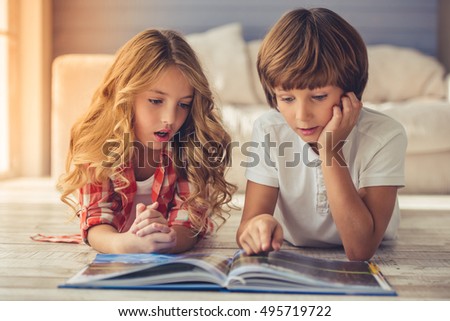 Pretty little girl and boy are reading book and showing surprise while lying on the floor at home