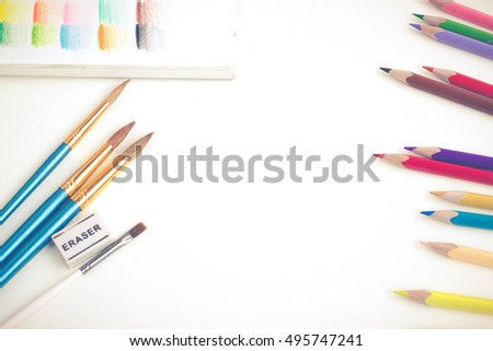 Top view of art supplies on white table. Colored pencils, paintbrushes and sketchbook.  May be used as product mockup.  Royalty-Free Stock Photo #495747241