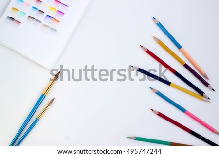 Top view of art supplies on white table. Colored pencils, paintbrushes and sketchbook.  May be used as product mockup.  Royalty-Free Stock Photo #495747244