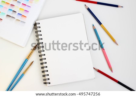 Top view of art supplies on white table. Colored pencils, paintbrushes and sketchbook.  May be used as product mockup.  Royalty-Free Stock Photo #495747256