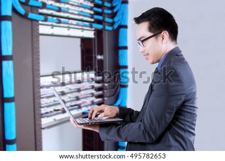 Young businessman working with a laptop computer near the network servers. Concept of network center