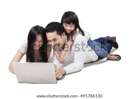 Picture of cheerful Asian family lying in the studio while browsing internet online with a laptop, isolated on white background