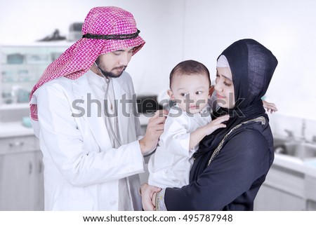 Picture of a male Arabian doctor examining a baby boy with a stethoscope in the clinic room