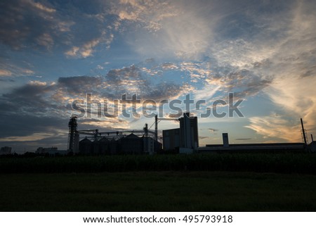 silhouette of factory during sunrise with yellow sky and clouds. Feed mills