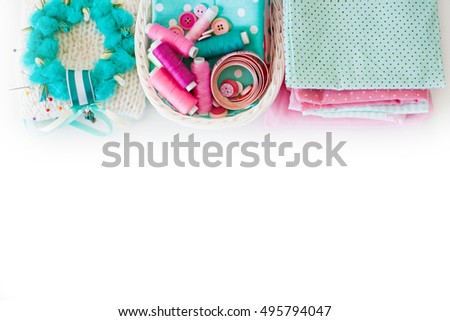 Accessories for sewing lie on a white background. Measuring tape, thread, fabric and needles for sewing. Fabric pink, mint, and turquoise.