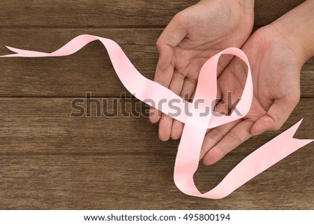 Pink ribbon symbol in hands placed on a wooden background. Pink ribbons Breast Cancer. Women healthcare