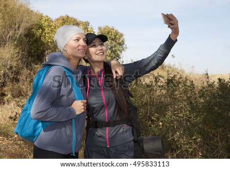 Two girls friends outdoors watching photos at digital camera  tourists laighing and having fun in summer park lifestyle portrait.