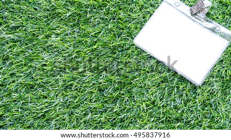 Name tag or identification holder with metal clip on greenish synthetic grass. Concept of garden wedding event or invitation. Slightly de-focused and close-up shot. Copy space.