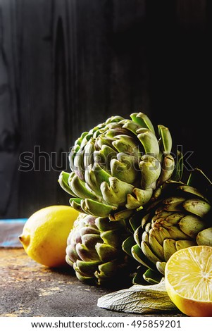 Baby ripping organic Artichokes in the rustic wooden board with lemon, solfetka. Dark background