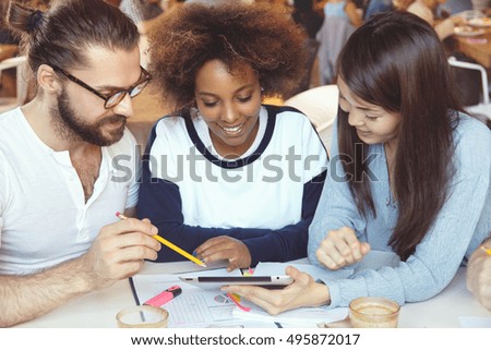 Brainstorm concept. Young colleagues of diverse ethnicities working together on common project, analyzing financial statistics and company's growth, making report at cafeteria, using touch pad pc