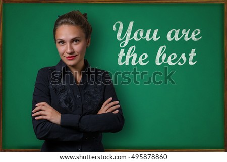 Beautiful young woman teacher (student, business woman) in classical dress standing near a blackboard with the inscription you are the best