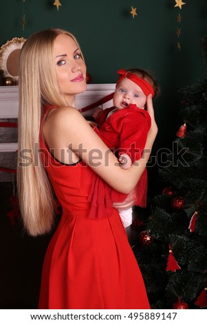tender photo of beautiful mother with luxurious blond hair posing with her cute little baby girl beside Christmas tree in cozy home  