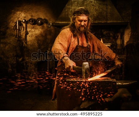 Senior blacksmith forging the molten metal on the anvil in smithy. Royalty-Free Stock Photo #495895225