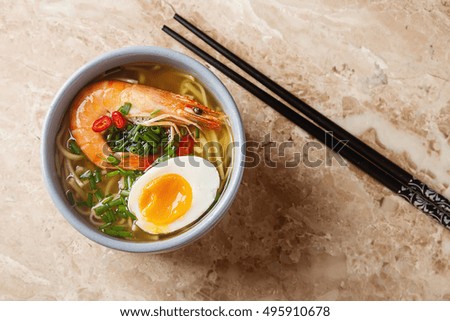 Miso Ramen Asian noodles with egg, shrimp, green onions, chili peppers in a white bowl. Bright marble background