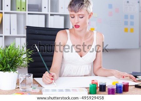 Woman painter in elegant top is doing her job at the office of company. Concept of creating beauty every day