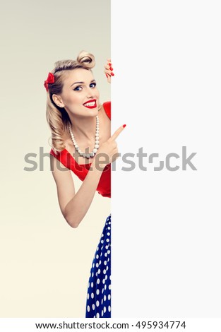 Smiling woman in pin-up style dress, showing blank signboard with copyspace area for advertising slogan or text message. Caucasian blond model posing in retro fashion and vintage concept studio shoot.