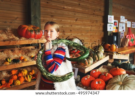 Adorable little girl of 8-9 year old choosing halloween pumpkin on farm market, having fun with unusual different kind of pumpkins