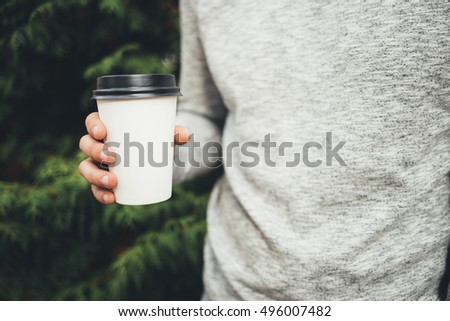 Man holding coffee to go while walking in the park, mock-up of coffee cup