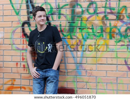 Teenage boy with ear-phones having fun, listen to music and relax over brick wall with graffito drawing, outdoor portrait Royalty-Free Stock Photo #496051870