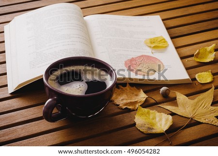 Cup of coffee, book and autumn leaves on the wooden table.