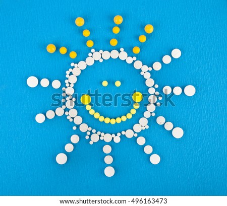 Many different colorful medication and pills from above in the shape of a cartoon sun on a blue background