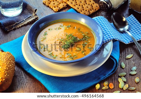 Pumpkin cream-soup. Hot pumpkin soup with sour cream with roasted sesame seeds in a blue bowl on a wooden table. Still life with a bowl of soup, spoon, pumpkin seeds and piece of bread and  baguette
